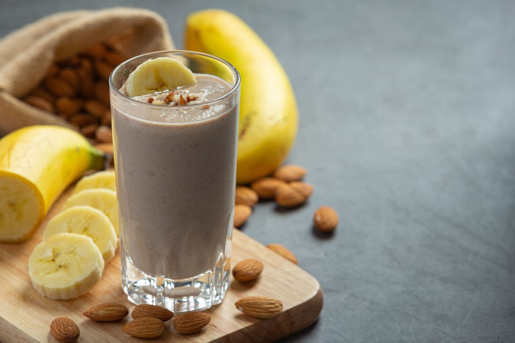 Bananen-Mandel-Smoothie auf Küchentheke neben Obst-Platter