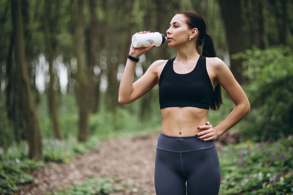 Frau im Wald joggend mit Protein-Shake